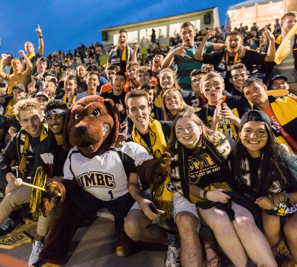 A crowd in the bleachers at a UMBC sports game with the UMBC mascot.